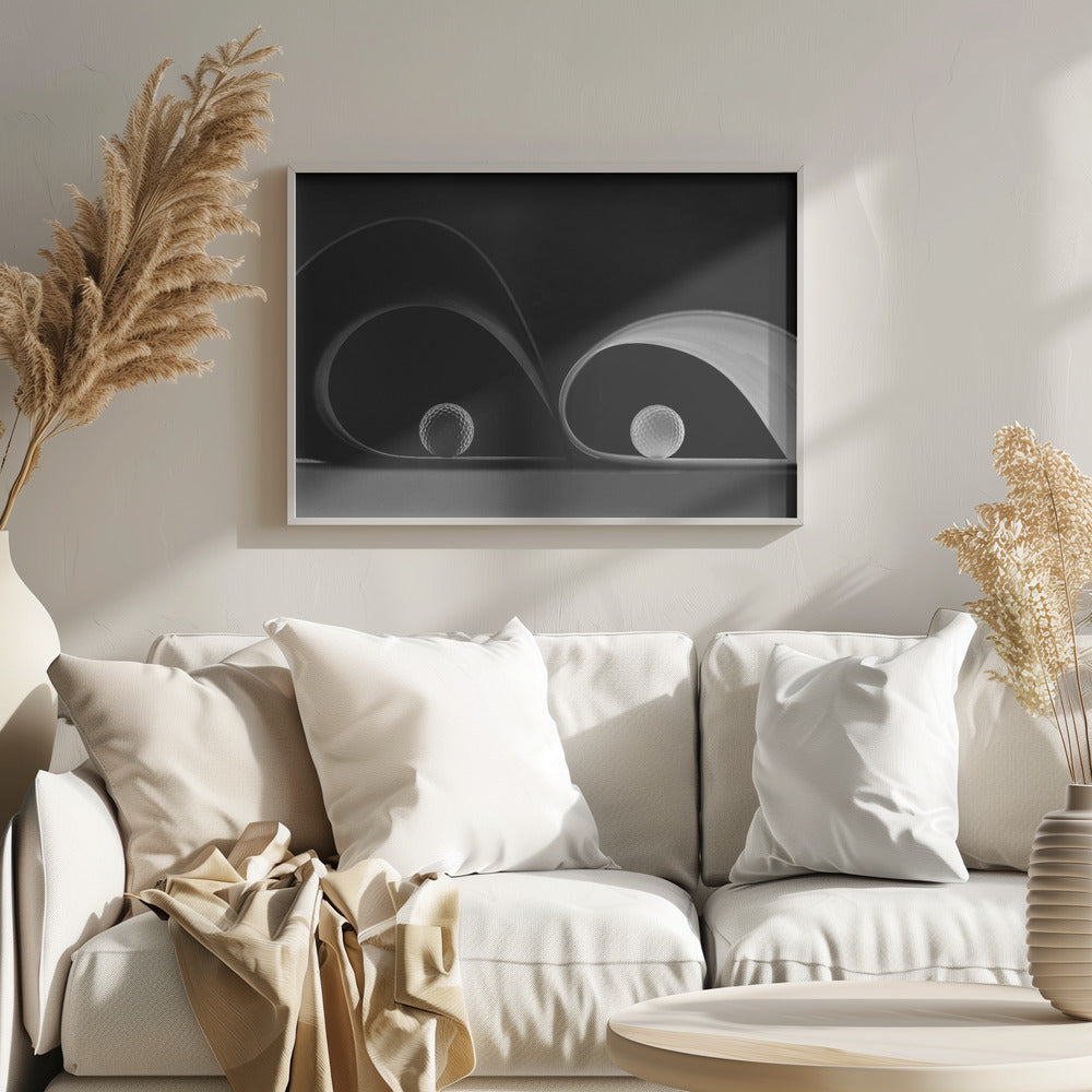 A framed, black and white abstract photograph featuring two golf balls nestled within the graceful curves of a single sheet of paper, creating a striking interplay of light, shadow, and form against a dark background. Decor
