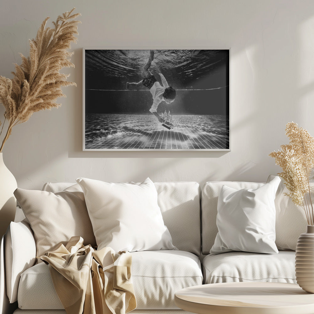 A surreal black and white underwater photograph of a child in a white shirt and shorts diving towards the bottom of a tiled pool to retrieve a miniature model of a sailing ship. Artwork