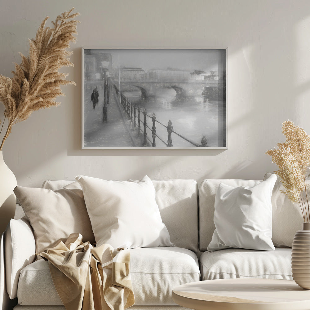 A framed, black and white impressionistic artwork of a city scene on a foggy or rainy day. In the foreground, a dark metal railing runs along a riverside walkway where a person in a dark coat is walking. An arched stone bridge crosses the river in the midground, with hazy buildings visible in the background, creating a moody and atmospheric scene. Wall Art