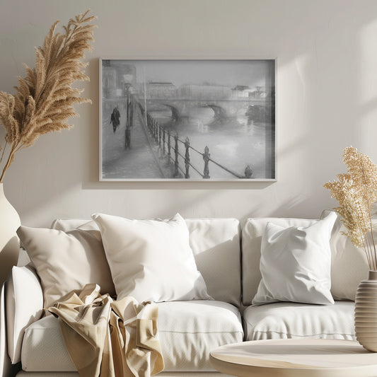 A framed, black and white impressionistic artwork of a city scene on a foggy or rainy day. In the foreground, a dark metal railing runs along a riverside walkway where a person in a dark coat is walking. An arched stone bridge crosses the river in the midground, with hazy buildings visible in the background, creating a moody and atmospheric scene. Wall Art