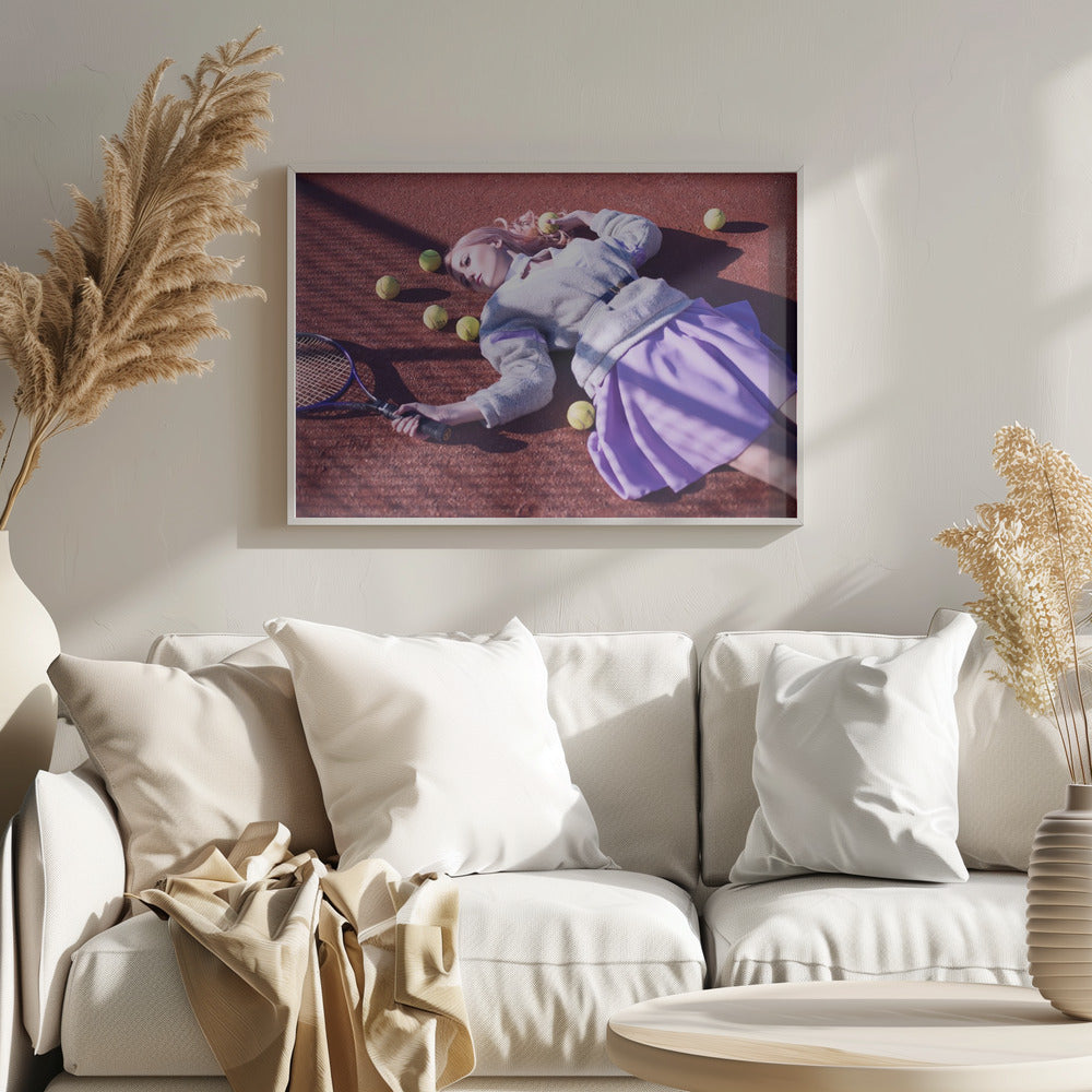 A high-angle shot of a young woman with pink hair lying on a red clay tennis court, surrounded by yellow tennis balls. She wears a grey sweater, a white collared shirt, and a purple pleated skirt, and holds a tennis racket in one hand. The scene is framed with a silver border. Wall Art