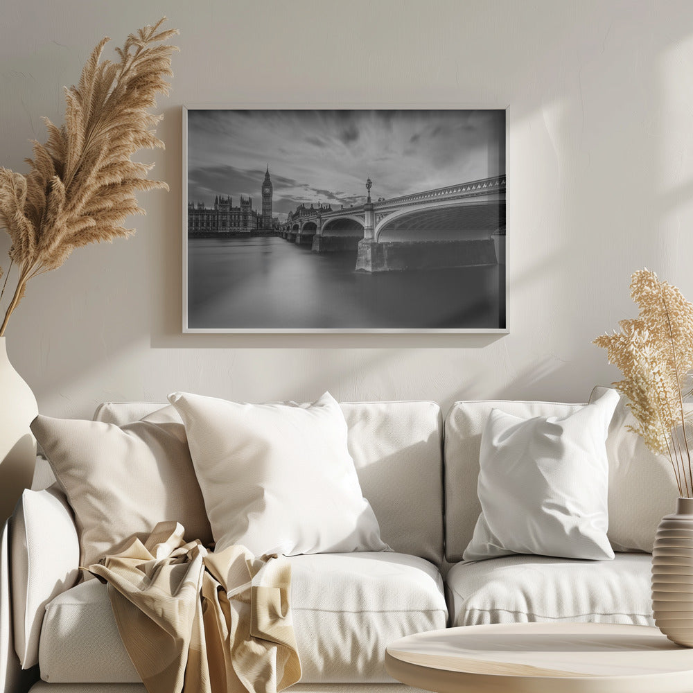 A dramatic black and white long-exposure photograph of London, featuring the smooth River Thames in the foreground, Westminster Bridge on the right, and the iconic Big Ben and Houses of Parliament on the left under a cloudy, streaked sky. The image is presented in a silver frame. Print
