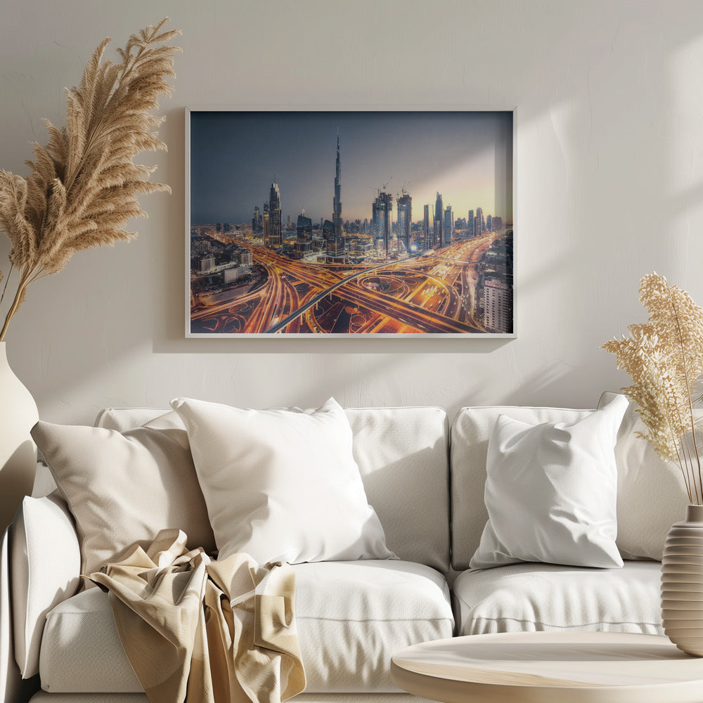 A wide-angle, elevated photograph of the Dubai skyline at dusk, with the iconic Burj Khalifa towering in the center. In the foreground, a complex network of highways glows with the orange light trails of moving traffic, while the city's numerous skyscrapers are illuminated against a twilight sky. Print