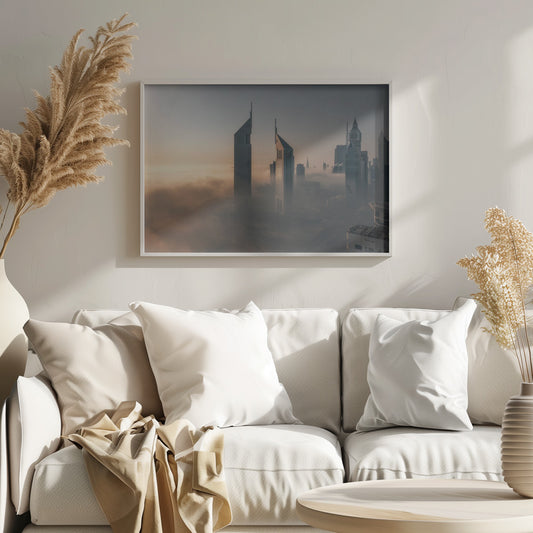 A framed aerial photograph of a futuristic city skyline, likely Dubai, enveloped in a thick layer of fog at sunrise. Tall, modern skyscrapers, including the iconic Emirates Towers, pierce through the clouds, with the warm light of the rising sun creating a hazy, golden glow on the left. Poster