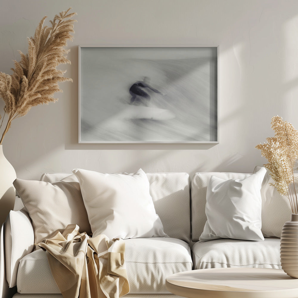 An artistic black and white photograph using motion blur to capture a surfer in a dynamic, fluid pose on a wave. The slow shutter speed creates a sense of speed and abstract movement, with the surfer's dark wetsuit contrasting against the white, streaked water. The image is presented in a silver frame. Decor