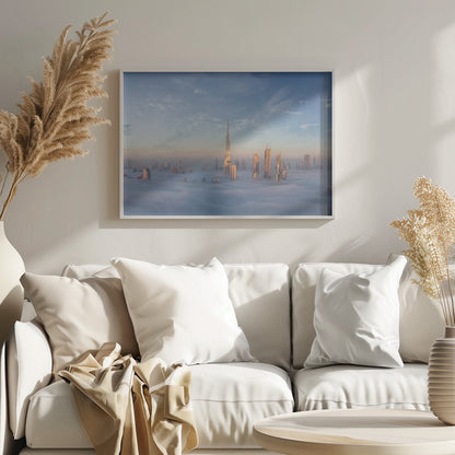 A framed photograph of the Dubai skyline, with the Burj Khalifa and other skyscrapers piercing through a thick blanket of low-lying clouds or fog. The scene is bathed in the warm, golden light of sunrise or sunset against a pale blue sky. Poster