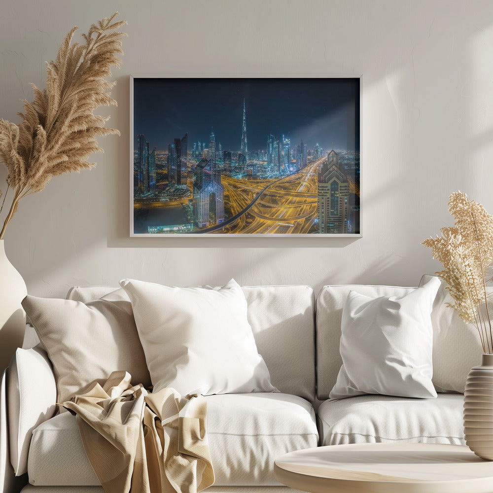 A vibrant aerial photograph of the Dubai skyline at night, with the iconic Burj Khalifa towering in the center. A complex web of brightly lit highways with light trails from traffic dominates the foreground, weaving between modern skyscrapers under a starry night sky. Decor