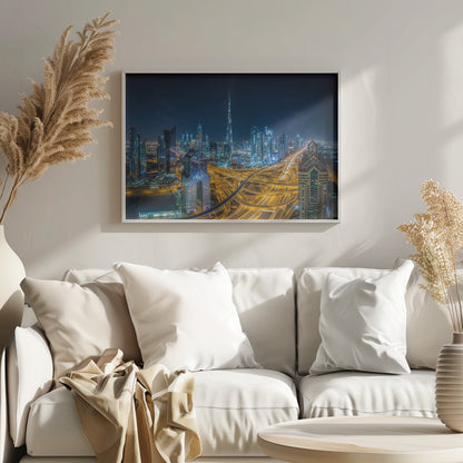 A vibrant aerial photograph of the Dubai skyline at night, with the iconic Burj Khalifa towering in the center. A complex web of brightly lit highways with light trails from traffic dominates the foreground, weaving between modern skyscrapers under a starry night sky. Decor