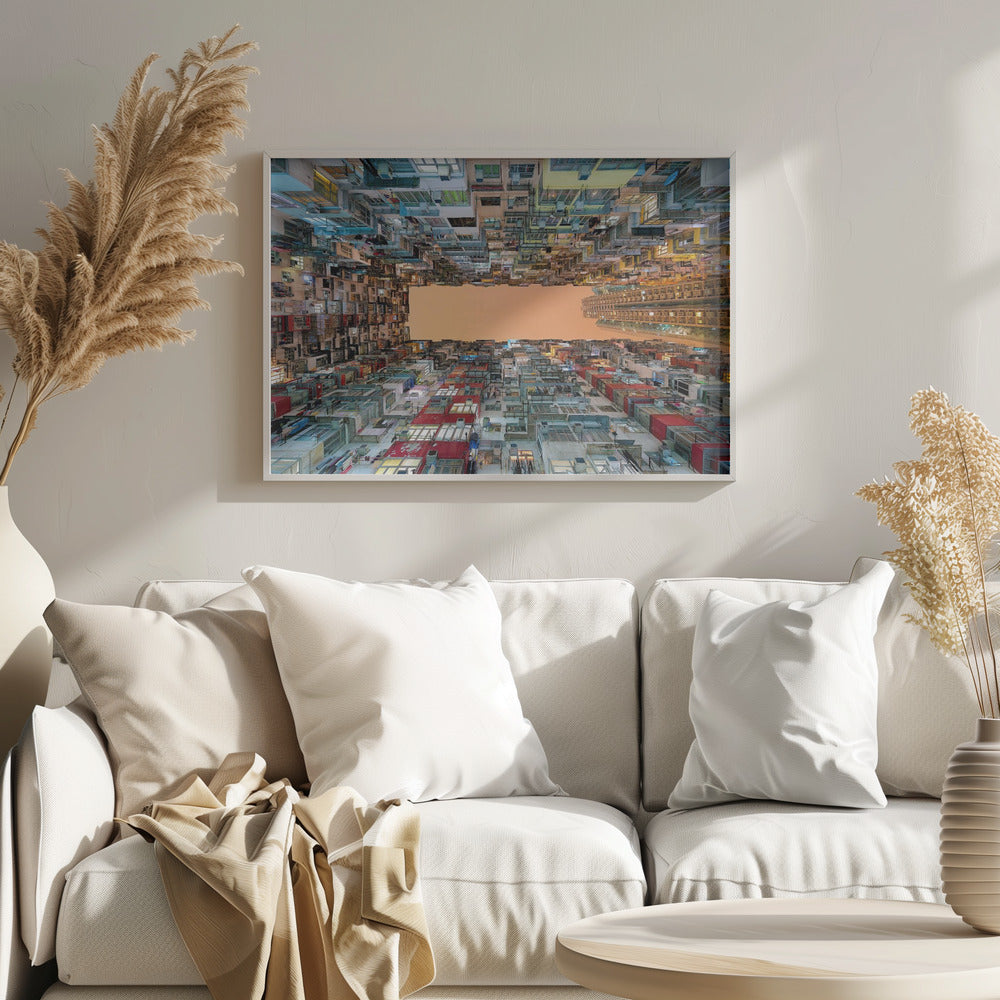 An upward-looking photograph from a courtyard surrounded by densely packed, multi-colored apartment buildings that create a rectangular frame around an orange sky. The unique perspective creates a surreal and geometric view of an urban landscape, all enclosed in a silver frame. Artwork