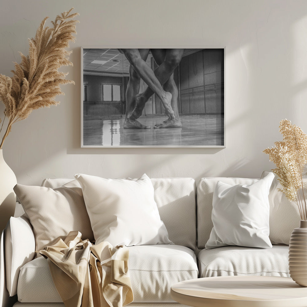 A dramatic low-angle, black and white photograph capturing the muscular legs and bare feet of two dancers intertwined in a dance studio. Their limbs cross in a display of strength and grace on a reflective wooden floor, with the studio's mirrored wall and barre visible in the background. The image is enclosed in a silver-grey frame. Decor