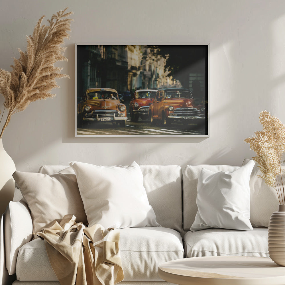 Three vintage American cars drive down a sunlit city street. The foreground features an orange taxi, with a red car and another orange vehicle behind it, all under the warm glow of late afternoon light casting long shadows. Print