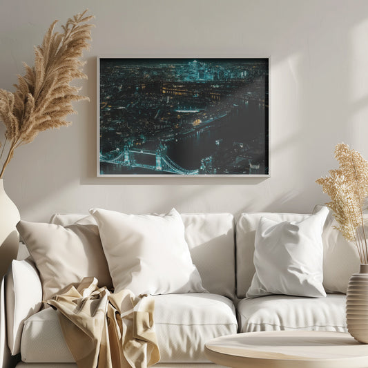 A framed aerial photograph of London at night, featuring the iconic Tower Bridge illuminated in bright teal in the foreground and the glowing skyscrapers of Canary Wharf across the River Thames in the background. Artwork