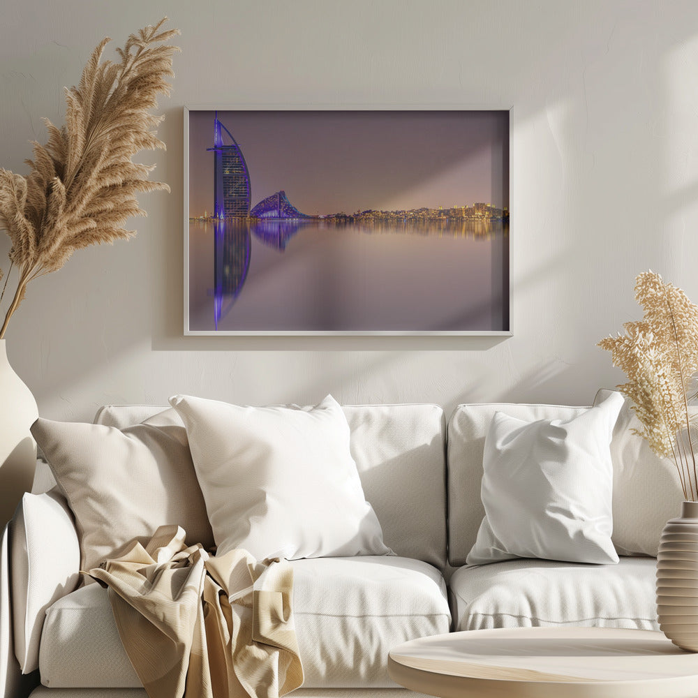 A framed panoramic night photograph of the Dubai skyline featuring the Burj Al Arab hotel lit up in brilliant purple. The city lights and architecture are perfectly reflected in the calm water in the foreground, all under a hazy, dusky sky. Poster