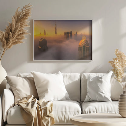 An aerial photograph of the Dubai skyline shrouded in a thick blanket of fog at sunrise. The warm golden light illuminates the tops of several skyscrapers, including the Burj Khalifa, which pierce through the clouds creating a dreamlike and majestic scene. Print
