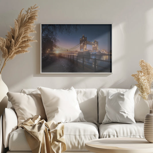 A scenic photograph of London's Tower Bridge at sunrise, its lights glowing warmly against a deep blue and orange sky. In the foreground, a cobblestone path follows the River Thames, leading the eye towards the iconic bridge and the rising sun. Poster