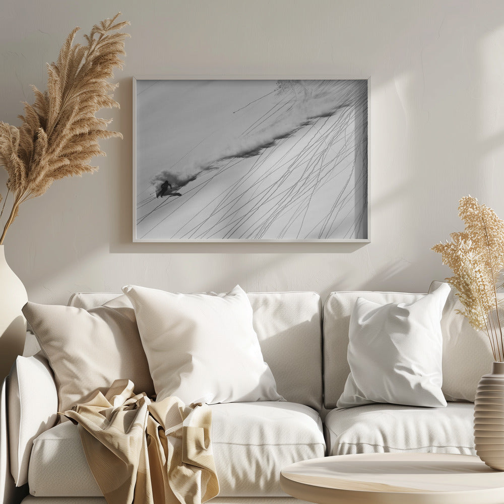A dramatic black and white overhead photograph of a skier carving down a steep, powder-filled mountain slope, kicking up a huge plume of snow. Numerous ski tracks crisscross the pristine white snow, creating a pattern of dark lines. Poster