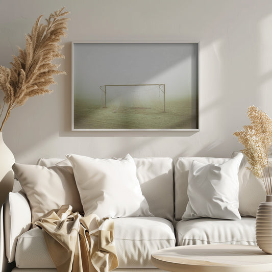A framed photograph of an empty soccer goal with a net, standing alone on a green grass field enveloped in thick, white fog, creating a minimalist and atmospheric scene. Poster