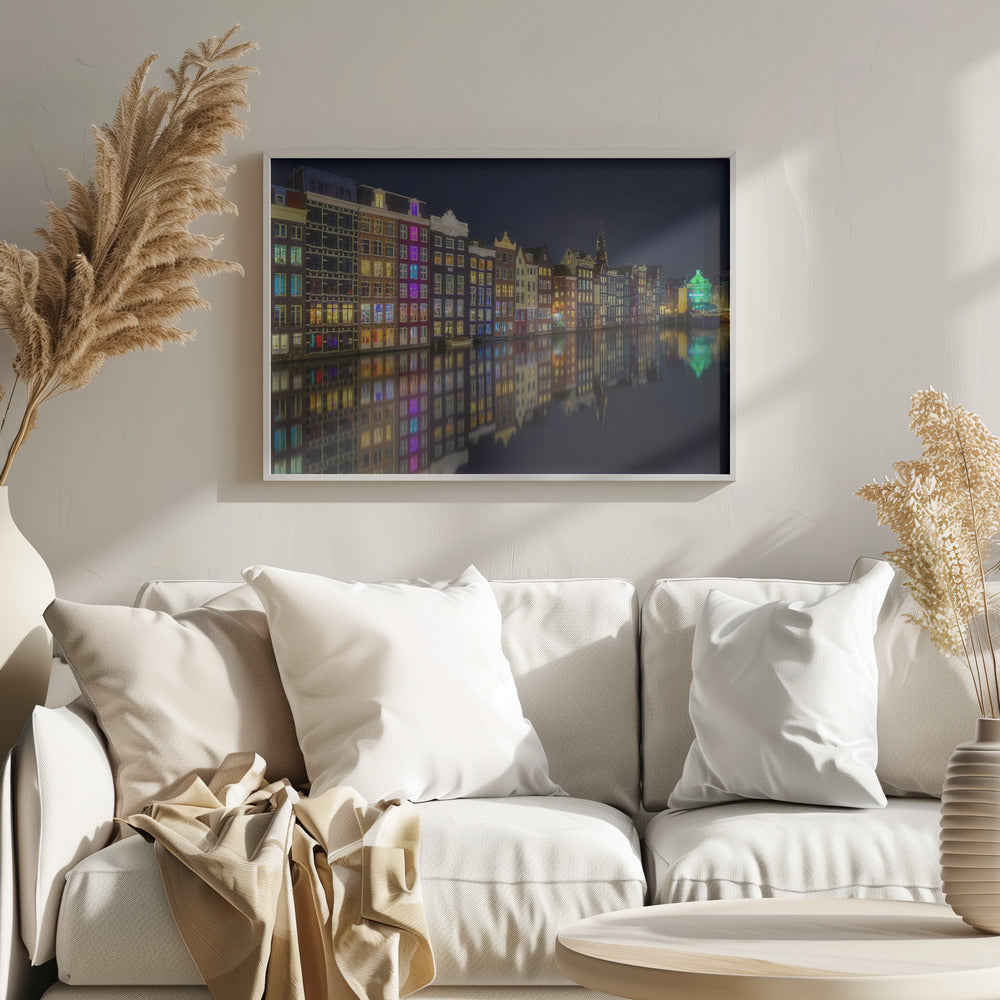 A vibrant nighttime photograph of colorful canal houses in Amsterdam, with their glowing lights beautifully reflected in the still water of the canal below, all framed in silver. Print