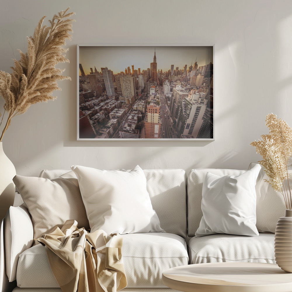 An aerial photograph of the New York City skyline at sunset, with the Empire State Building prominent against the glowing sky. The warm light of the setting sun bathes the dense urban landscape in a golden hue. The entire scene is enclosed in a silver, brushed metal frame. Print