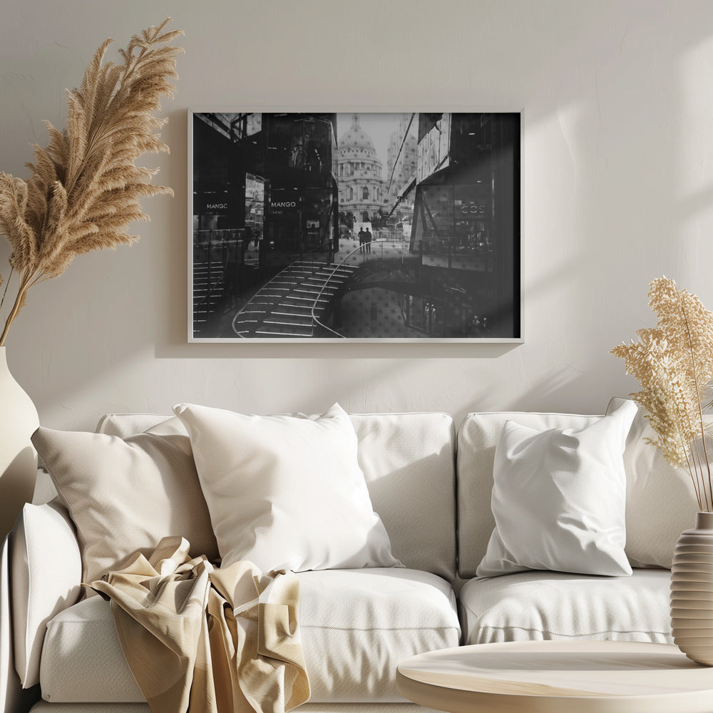 A framed, black and white photograph capturing a layered urban scene. The view, seen through a window with reflections of a curved, lit staircase, shows two people walking towards a large domed cathedral framed by modern glass buildings. Wall Art