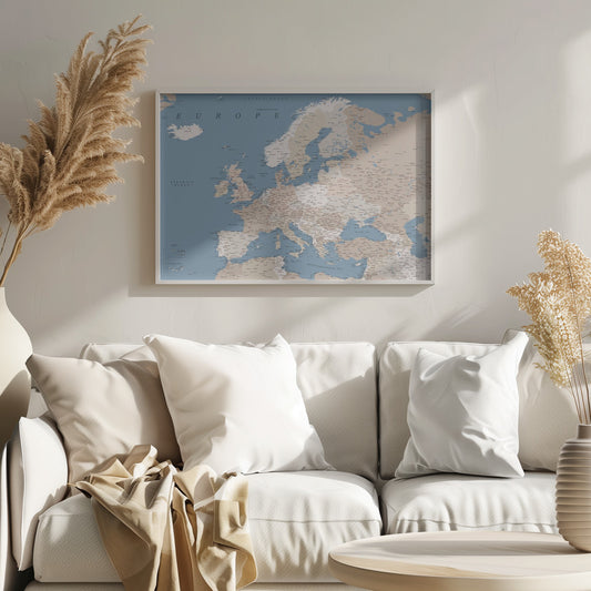 A detailed, framed map of Europe with a muted color palette. The oceans and seas are a soft blue, while the countries are various shades of beige and tan. Text labels for countries, cities, and bodies of water are clearly visible across the map. The map is housed in a simple silver-gray frame. Poster