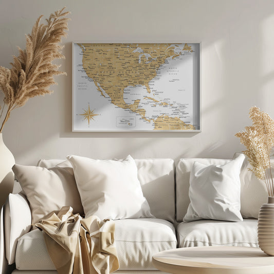 A stylized map of North and Central America and the Caribbean, featuring gold-colored landmasses on a light gray, textured background. Countries, states, and major cities are labeled in black text. A compass rose is shown in the lower-left corner. The entire map is enclosed in a light gray frame. Decor