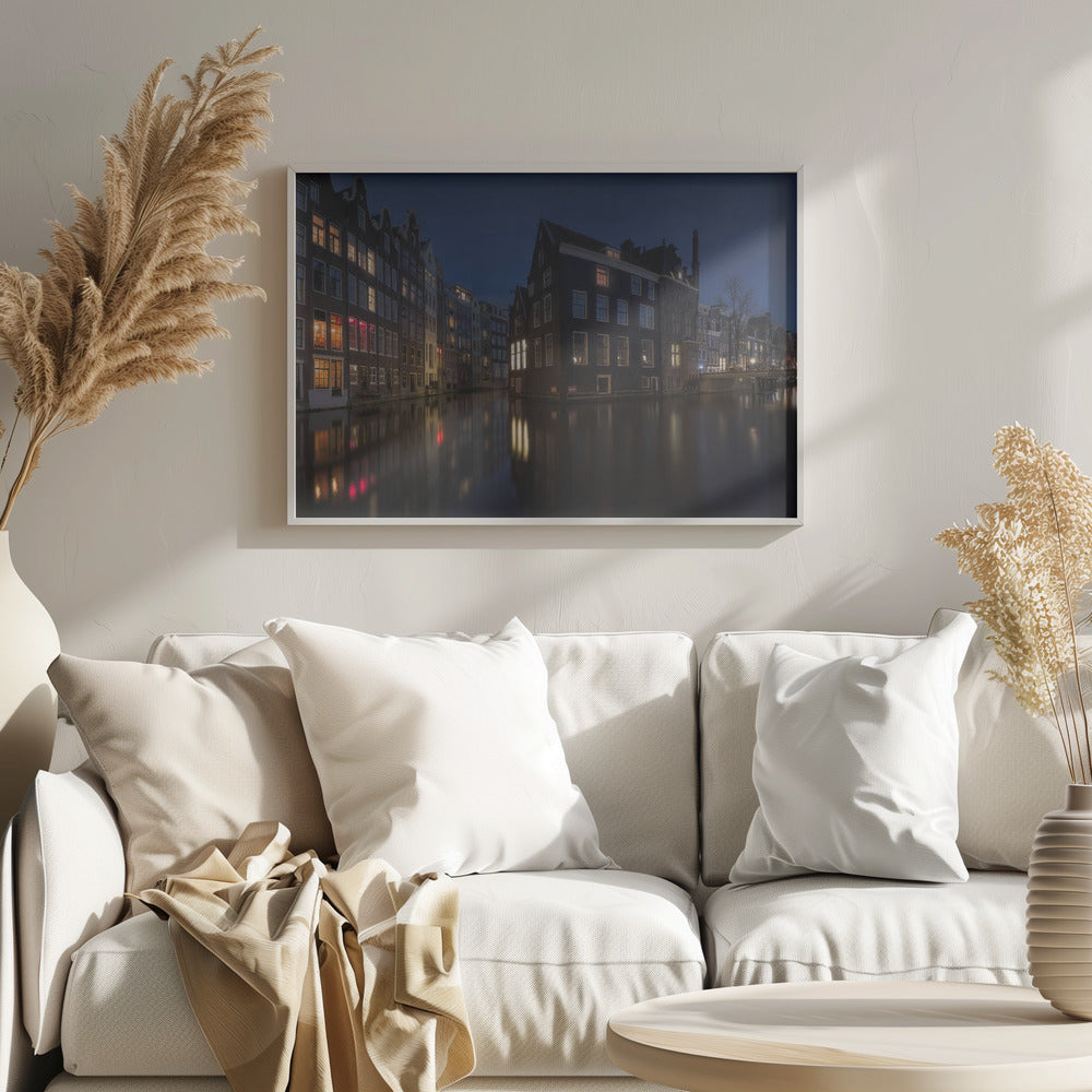 A framed photograph capturing a serene night view of an Amsterdam canal. Traditional Dutch houses with lit windows line the calm water, casting warm reflections under a deep blue twilight sky. Wall Art
