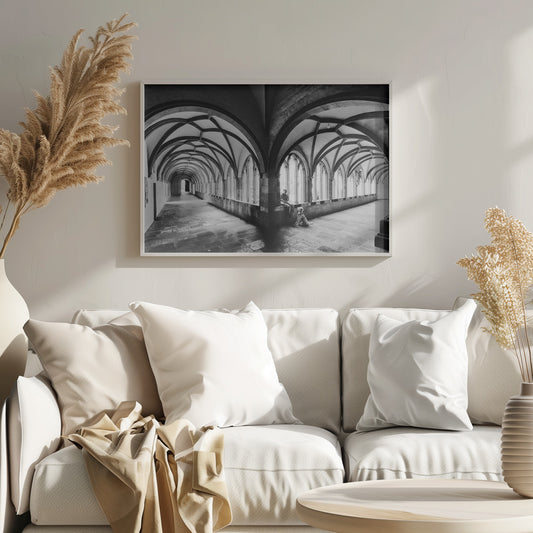 A black and white photograph of a person and their dog sitting in the corner of a Gothic cloister. The stone hallway features a dramatic vaulted ceiling and a long row of arched windows, creating a powerful sense of perspective and light. Decor