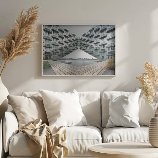 A symmetrical, mirrored photograph of a modern V-shaped apartment complex with numerous glass balconies, overlooking a wooden deck and a calm body of water under a grey sky. The image is presented within a silver picture frame. Artwork