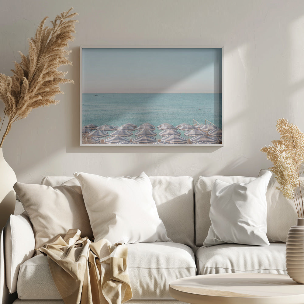 A high-angle photograph of a beach packed with blue and white striped umbrellas, with the turquoise ocean stretching out to a pale blue sky in the background. The entire image is enclosed in a silver frame. Poster
