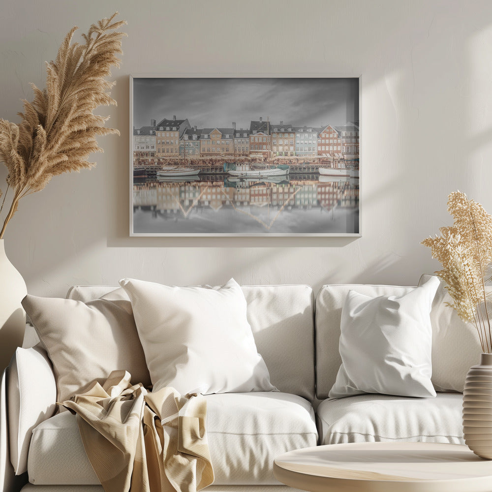 A framed, color-selective photograph of the Nyhavn harbor in Copenhagen. A row of colorful 17th and 18th-century townhouses lines the waterfront, with their warm lights and facades reflecting in the calm canal. The sky and parts of the water are in black and white, making the colored buildings stand out. Several boats are moored along the quay. Decor