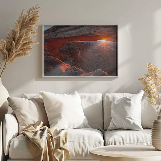 A spectacular sunrise seen through the natural frame of Mesa Arch in Canyonlands National Park, Utah. The sun bursts over the horizon, casting a dramatic orange and red glow on the underside of the rock arch and the vast canyon landscape below. Poster