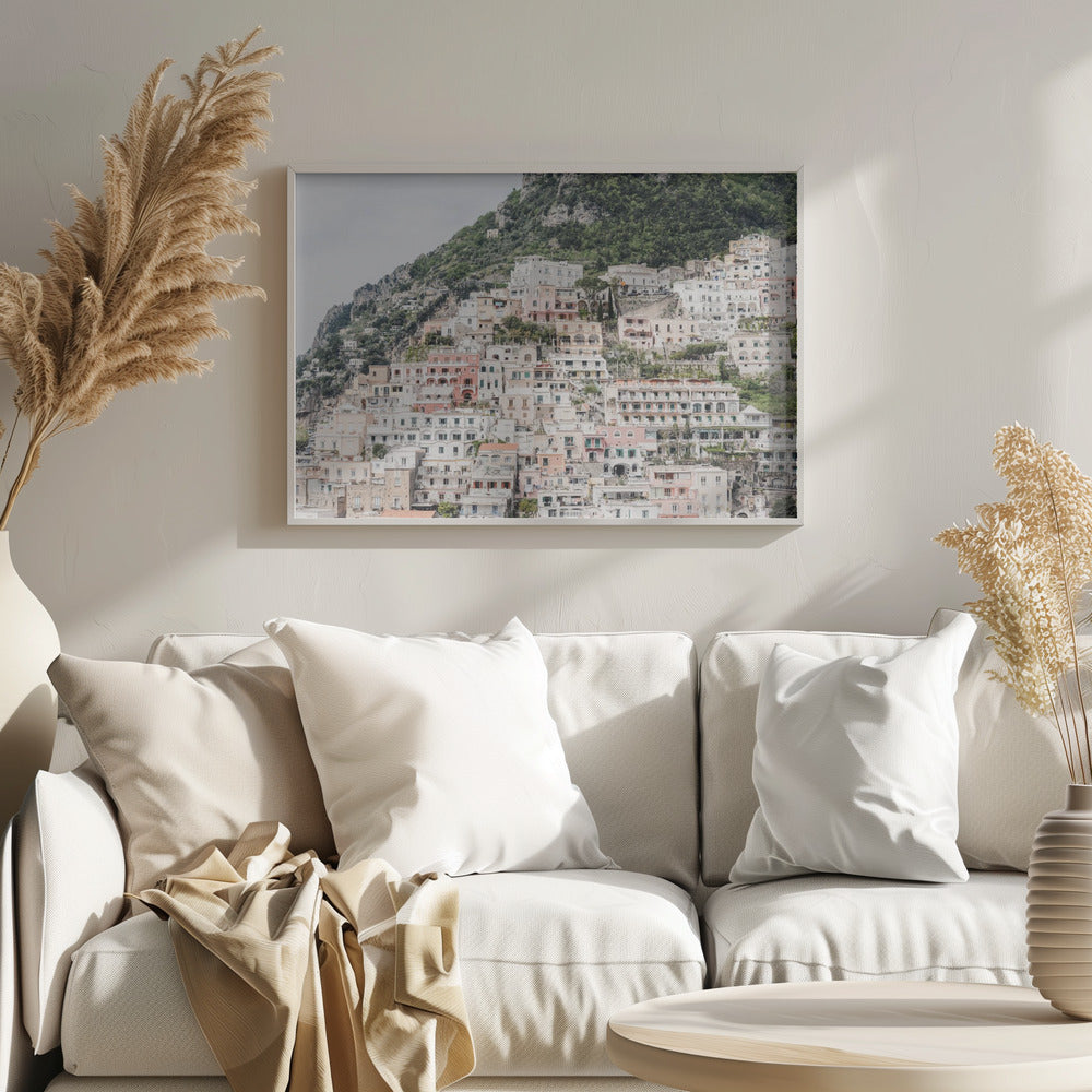 Photograph of the iconic cliffside village of Positano on the Amalfi Coast, showcasing a dense cascade of white, pink, and peach buildings down a lush green mountain under an overcast sky. The image is presented within a silver picture frame. Artwork
