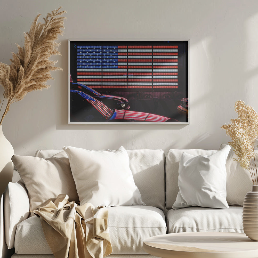 A large illuminated American flag on a billboard at night, with its red, white, and blue lights reflecting on the glossy hoods of two cars in the foreground. Wall Art