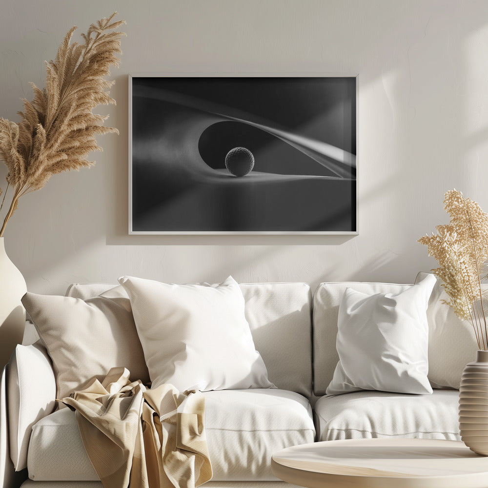 An artistic black and white photograph of a golf ball resting inside the gentle curve of a dark, abstract shape, creating a minimalist and dramatic composition with strong light and shadows. Poster