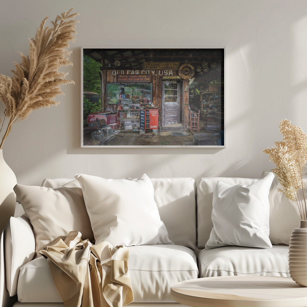 A framed photograph of the cluttered entrance to a rustic wooden building labeled 'Old Car City, USA'. The scene is filled with vintage memorabilia, including car parts, old signs, a red Coca-Cola cooler, and the weathered door to an office. Poster