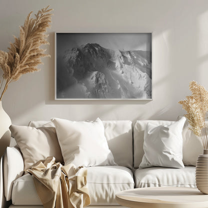 A dramatic black and white photograph of a person standing alone on the ridge of a massive, snow-covered mountain, emphasizing the scale and solitude of the vast, rugged landscape, all presented in a silver frame. Wall Art