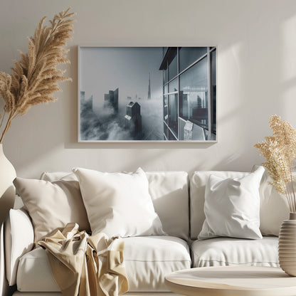 A framed black and white photograph with a cool blue tint, depicting the Dubai skyline from a high-rise window, with skyscrapers including the Burj Khalifa piercing through a thick blanket of fog. Artwork