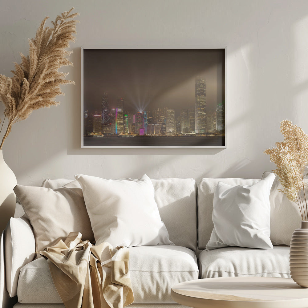 A framed photograph of the Hong Kong skyline at night, viewed from across the water. The skyscrapers are brilliantly lit with yellow, white, and colorful lights, and beams of light shoot up into the foggy, glowing sky. Decor