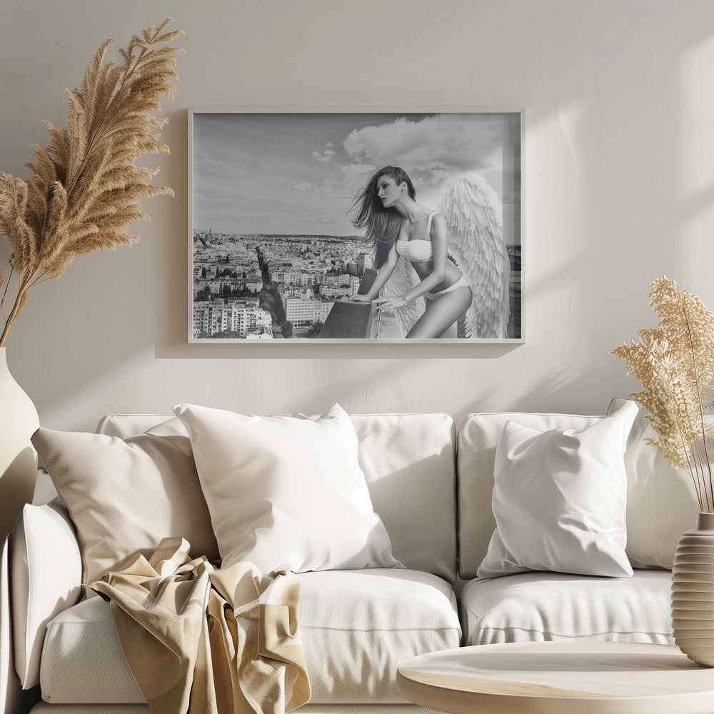A framed black and white photograph of a woman with large angel wings wearing white lingerie, looking out over a cityscape from a high vantage point. Her long dark hair is blowing in the wind, and the sky is filled with clouds. Poster