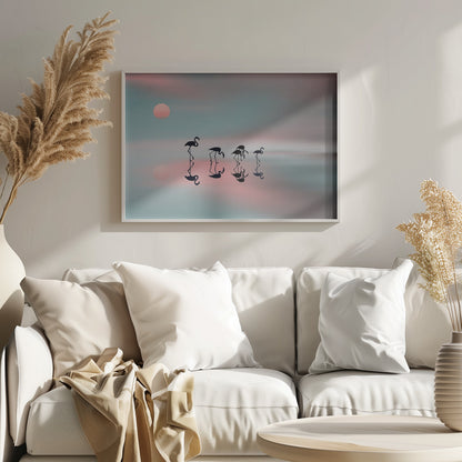 A serene artwork of five black flamingo silhouettes wading in calm water, their reflections mirrored below them. The background is a soft, blurred gradient of pastel pink and teal, with a pale pink sun low in the sky, creating a tranquil sunset scene. Poster