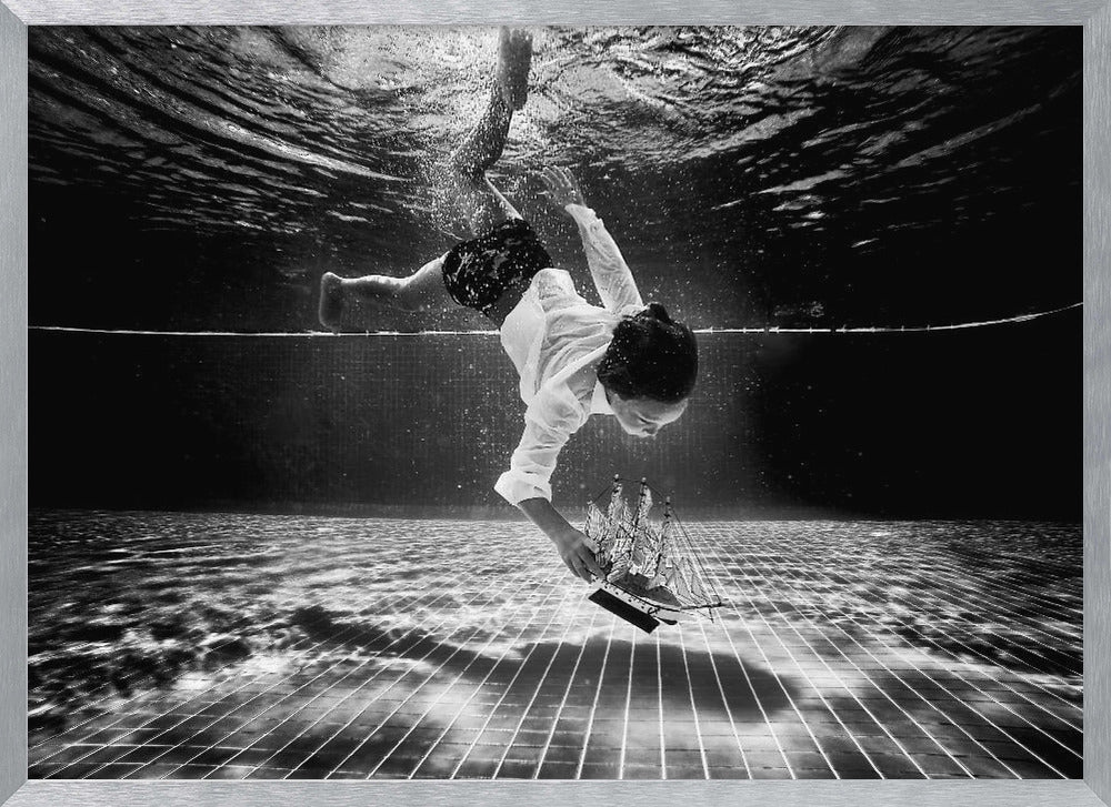 A surreal black and white underwater photograph of a child in a white shirt and shorts diving towards the bottom of a tiled pool to retrieve a miniature model of a sailing ship. Artwork
