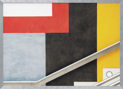 A framed abstract art piece featuring a composition of large, solid-colored geometric shapes in red, yellow, black, white, and light gray. A silver handrail cuts diagonally across the lower portion of the image, adding a sharp line and a sense of architectural space. Artwork