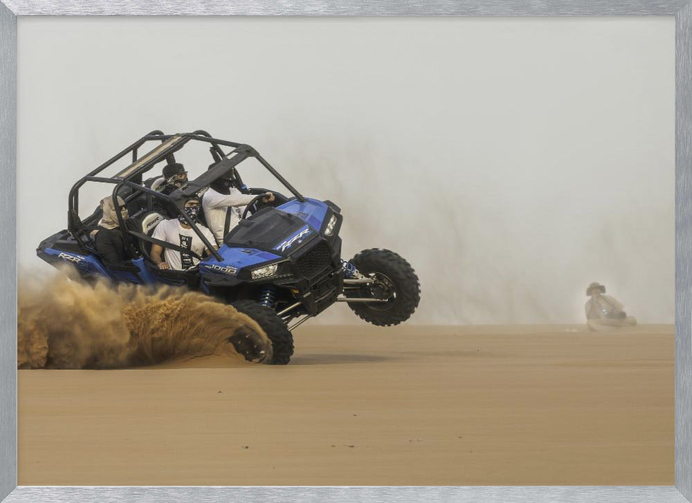 A framed action shot of a blue dune buggy with several passengers making a sharp turn in the desert, kicking up a large cloud of sand and lifting its front wheel off the ground. Wall Art