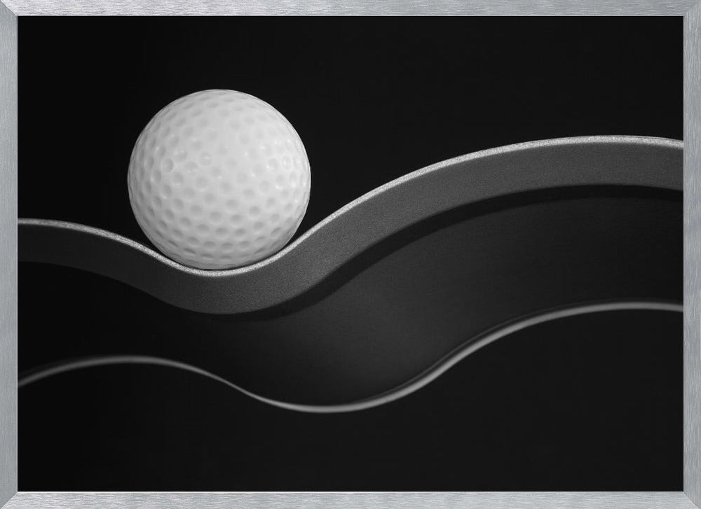 A framed, minimalist black and white photograph of a golf ball resting on a gracefully curving gray surface against a solid black background. Wall Art
