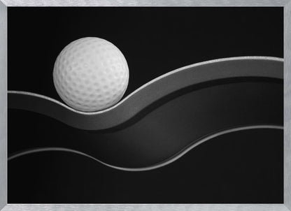 A framed, minimalist black and white photograph of a golf ball resting on a gracefully curving gray surface against a solid black background. Wall Art