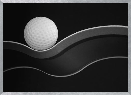A framed, minimalist black and white photograph of a golf ball resting on a gracefully curving gray surface against a solid black background. Wall Art