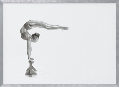 A framed black and white photograph of a female gymnast with a metallic silver-painted body, balancing in a difficult handstand pose on small blocks against a stark white background. Her back is arched and her legs are extended straight out behind her, parallel to the ground. Artwork
