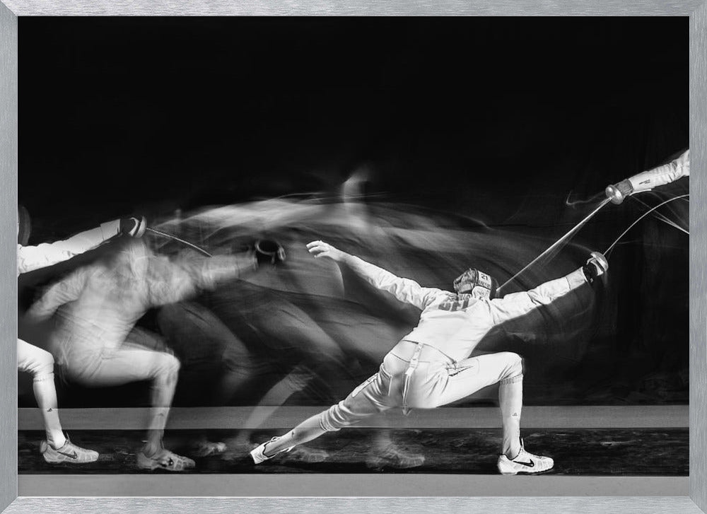 A framed, dramatic black and white photograph using long exposure to capture a fencer in motion. The fencer, in full white gear, lunges forward, their form crisp at the end of the movement while a ghostly blur trails behind, illustrating their rapid advance against a black background. Decor