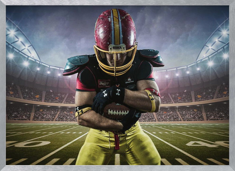 A framed poster of a determined football player in a red and yellow uniform standing on a field in a packed stadium. He is holding a football close to his chest with his head bowed, under bright stadium lights. Decor